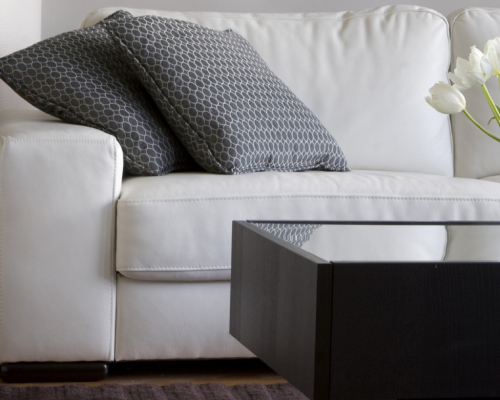 Image of a clean, white couch and two pillows behind a coffee table.