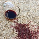 Spilled wine and wine glass on a white carpet to help illustrate does carpet cleaning remove stains.
