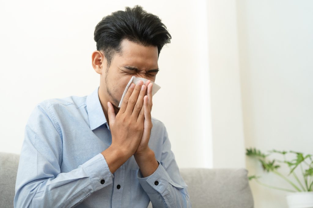Image of a person sneezing into a tissue to illustrate how to remove allergens from carpet.