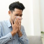 Image of a person sneezing into a tissue to illustrate how to remove allergens from carpet.